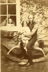 Padre e hija sentados en un caballo mecedor con el hermano y la madre mirando por la ventana, 1860s