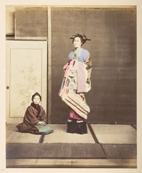 [? Geisha, ] Retrato de estudio de pie de cuerpo entero de una mujer joven con zapatos elevados, su joven asistente arrodillada en el suelo junto a ella,   Fotógrafo: Desconocido  Colección Lucas: Registro fotográfico de la gira mundial de Charles James y 