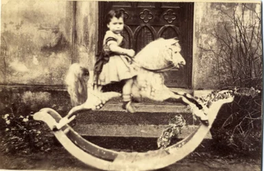 Niña pequeña en un gran caballo mecedor en un jardín, 1860s