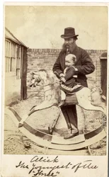 Niña en un caballo balancín en el jardín, su padre al lado