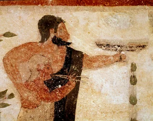 Un hombre barbudo presentando una copa, cerca de él un músico (detalle)