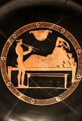 Copa: simposiata y joven esclava tocando el doble aulos (Cerámica de figuras rojas,)