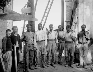 El equipo de carpinteros, trabajando en la restauración de la Abadía de Septfontaines, Bourmont en Haute-Marne, posando con sus herramientas, hacha, sierra, plomada, reglas y maza, alrededor de 1890. Fotografía. Colección Ducos