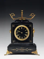 Reloj de sobremesa de piedra negra con decoración incisa, con patas, remates y accesorios en latón dorado, por Jausions de Pau, Francia, c.1876-78