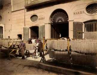 Filas de secadores de macarrones frente a una fábrica en Torre Annunziata. La escena está animada por los empleados de la fábrica de pasta: algunos posan, en primer plano, cerca de los secadores, otros están en el umbral de las entradas a la fábrica