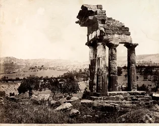 Vista de las cuatro columnas restantes que sostienen un entablamento del Templo de Cástor y Pólux en el Valle dei Templi, Agrigento. Un panorama de la ciudad es visible al fondo
