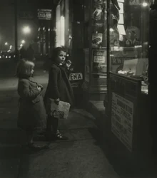 Dos niñas con abrigos de invierno en la puerta de una tienda por la noche