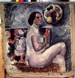 Desnudo. Retrato de una mujer desnuda, sentada con las piernas cruzadas, de perfil, esbozando un gesto de pudor. Detrás de ella, un cuadro de frutas y, colgado en la pared, un sombrero decorado con frutas. Pintura de Ilya Ivanovich Mashkov (Ilia Machkov