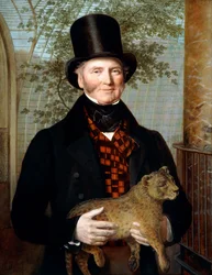Retrato de Edward Cross, de medio cuerpo, con abrigo negro y chaleco de cuadros rojos, sosteniendo un cachorro de león