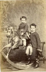 Niña en caballo de balancín con niño en falda escocesa de pie, 1860s