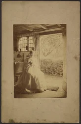 [Mujer con vestido largo a rayas sentada dentro de la habitación]