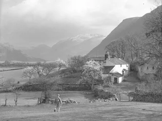Un hombre camina hacia un sendero y la casa de Gillerthwaite, con el lago y las colinas al fondo.