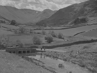 Vista de un puente, un arroyo, campos y colinas