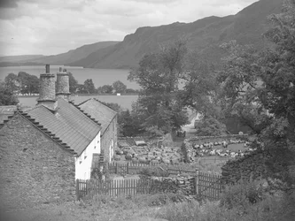 Edificios de granja con ovejas en el corral y Ullswater al fondo