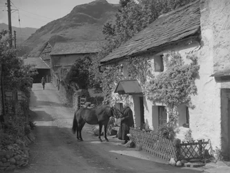 Anciana acariciando a un caballo que está parado en la carretera frente a una casa de campo.