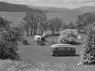 Tiendas y caravanas instaladas en un campo de Wastwater, con el lago y las colinas al fondo.
