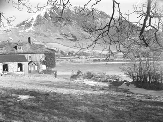 El Anglers Hotel de Ennerdale con árboles en primer plano y el lago helado y las colinas nevadas más allá.
