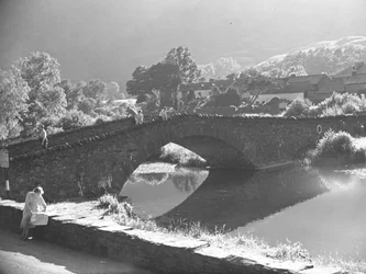Mujer sentada en la pared estudiando un mapa con un río y un puente de piedra al fondo