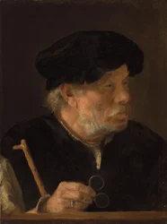 Un hombre, busto, sosteniendo un bastón y sus gafas, junto a un borde de madera