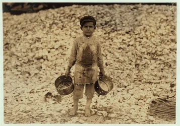Manuel, recolector de camarones migrante de 5 años, frente a un montón de conchas de ostras, trabajando por segundo año en Dunbar, Lopez, Dukate Company, Biloxi, Mississippi, 1911