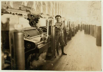 Niño barrendero junto a máquinas de cardado en Lincoln Cotton Mills, Evansville, Indiana, descalzo en un suelo resbaladizo, 1908