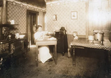 Mujer insertando cerdas en cepillos de dientes en su cocina, c.1912