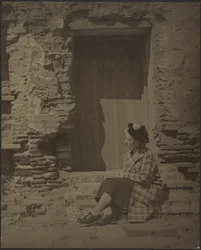 [Mujer sentada ante edificio en deterioro]