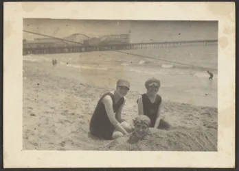 [Mujeres en la playa enterrando a una amiga en la arena]