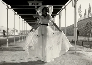 Modelo en un vestido de verano completo creado por la casa de alta costura "Graldi". El vestido es de una tela ligera decorada con bordados; un sombrero de ala ancha completa el conjunto.
