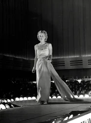 Modelo fotografiada en una pasarela con vestido de noche con tirantes de pedrería; el artículo es una creación de la casa de alta costura "Fumach".