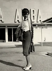 Modelo lleva conjunto creado por la casa de alta costura "Graldi". El atuendo se compone de un traje con blusa de dos tonos. Un sombrero rígido completa el conjunto.