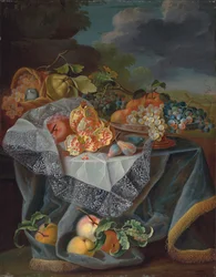 Uvas, peras y una manzana en un recipiente de vidrio, granadas y una cesta tejida con frutas en una mesa cubierta, y un paisaje de parque más allá