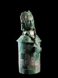 Vaso cilíndrico con mosaico de jadeíta, la tapa es una cabeza de hombre con tocado de plumas. De Tikal, c. 250 a 900