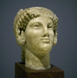 Cabeza de niña (Kore), escultura del período helenístico romano (siglo III-II después de nuestra era), rostro muy expresivo, pómulos prominentes hacia el este, sonrisa, cabello rizado, estilo arcaico de Ionia en el siglo VI antes de nuestra era que se perp