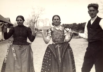 Dos damas y un hombre, vestidos con trajes tradicionales húngaros, bailan cogidos de la mano, con unas velas en las manos