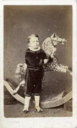 Niño pequeño de pie junto a un caballo de juguete