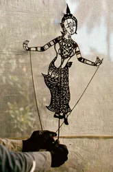 Un titiritero manipula una marioneta de sombras narrativa ante una pantalla para un teatro de sombras. C…