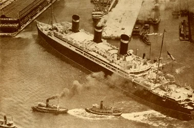 Fotografía aérea del Leviathan siendo remolcado por pequeños remolcadores a su muelle en Nueva York, c1930