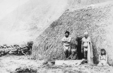 Una anciana golpeando tapa frente a una casa de hierba pili, Kalaupapa, Hawái, siglo XIX