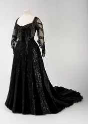 Vestido de noche negro de cuerpo entero usado por la reina Alejandra, con decoración de cuentas y lentejuelas e incorporando la característica cinta de seda negra con letras doradas del nombre de la reina Alejandra, confeccionado por Barolet de