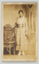 Tarjeta postal fotográfica de una mujer junto a una silla de madera, 1904-1918