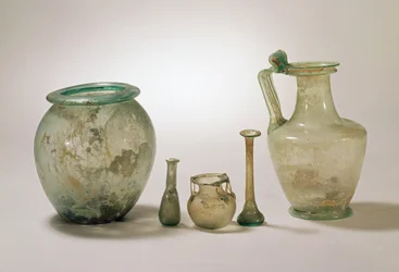 Colección de vidrio romano: urna cineraria, cristalería funeraria y jarra, siglos I-IV