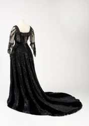 Vestido de noche negro largo usado por la reina Alejandra, con decoración de cuentas y lentejuelas e incorporando la característica cinta de seda negra de la reina Alejandra con su nombre en letras doradas, realizado por Barolet of Knightsbridge, Londres