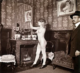 Fotografía enigmática que muestra a una joven completamente desnuda (salvo sus zapatos y medias) arreglándose el cabello ante un espejo en presencia de un hombre vestido y con sombrero. Podría pensarse que fue una foto tomada en un burdel, pero esta hip