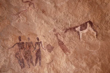 Arte rupestre, Prehistoria: Pintura rupestre de un grupo de personajes y una vaca bicolor con grandes cuernos en un refugio ornamentado, en el macizo de Uweinat, Egipto. (Período de 8000 a 3000 años a.C.). Fotografía