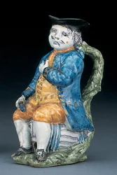 Jarra Toby con cara y manos de manganeso pálido, sosteniendo una jarra globular vacía de color buff en chaqueta y calzones azules lavados, y chaleco verde, c.1800