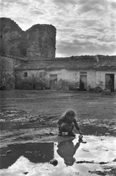 Niña joven jugando con un barco de papel en un charco rodeado de barro, Venosa, Basilicata, Italia