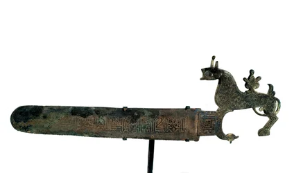 Sierra de bronce con la hoja decorada con inscripciones. Mango en forma de animal