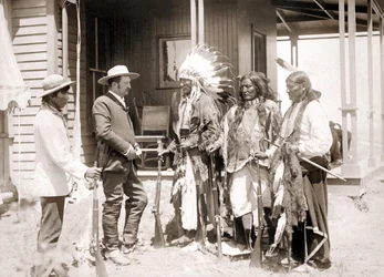 Tres Cheyenne vestidos con traje ceremonial y portando armas saludan a un Blanco acompañado de un intérprete. Finales del siglo XIX