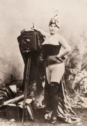 Retrato de una mujer parcialmente desnuda apoyada en una cámara antigua.